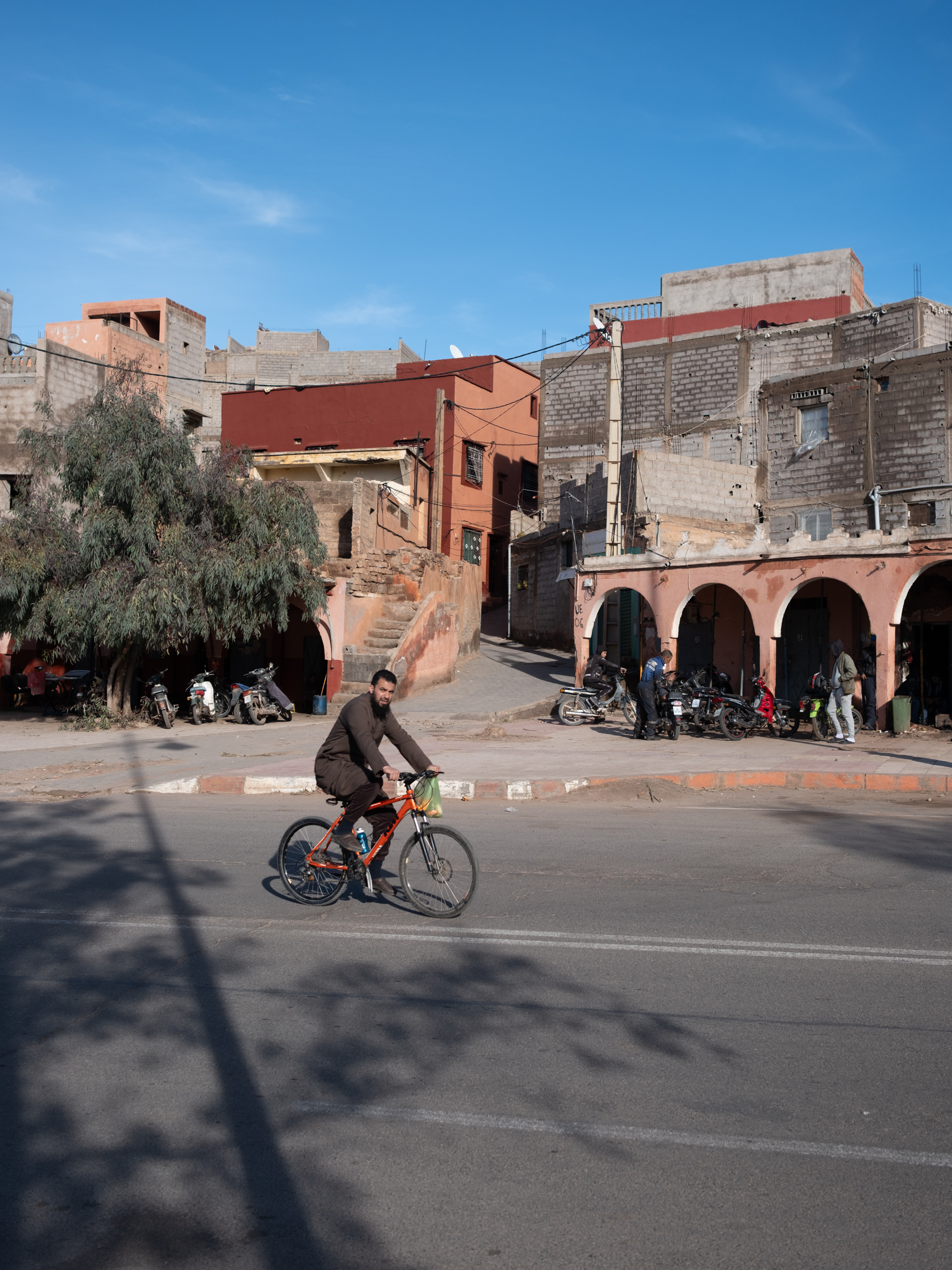 Man riding a bicycle on a street in a village, with clear blue sky and stone buildings.