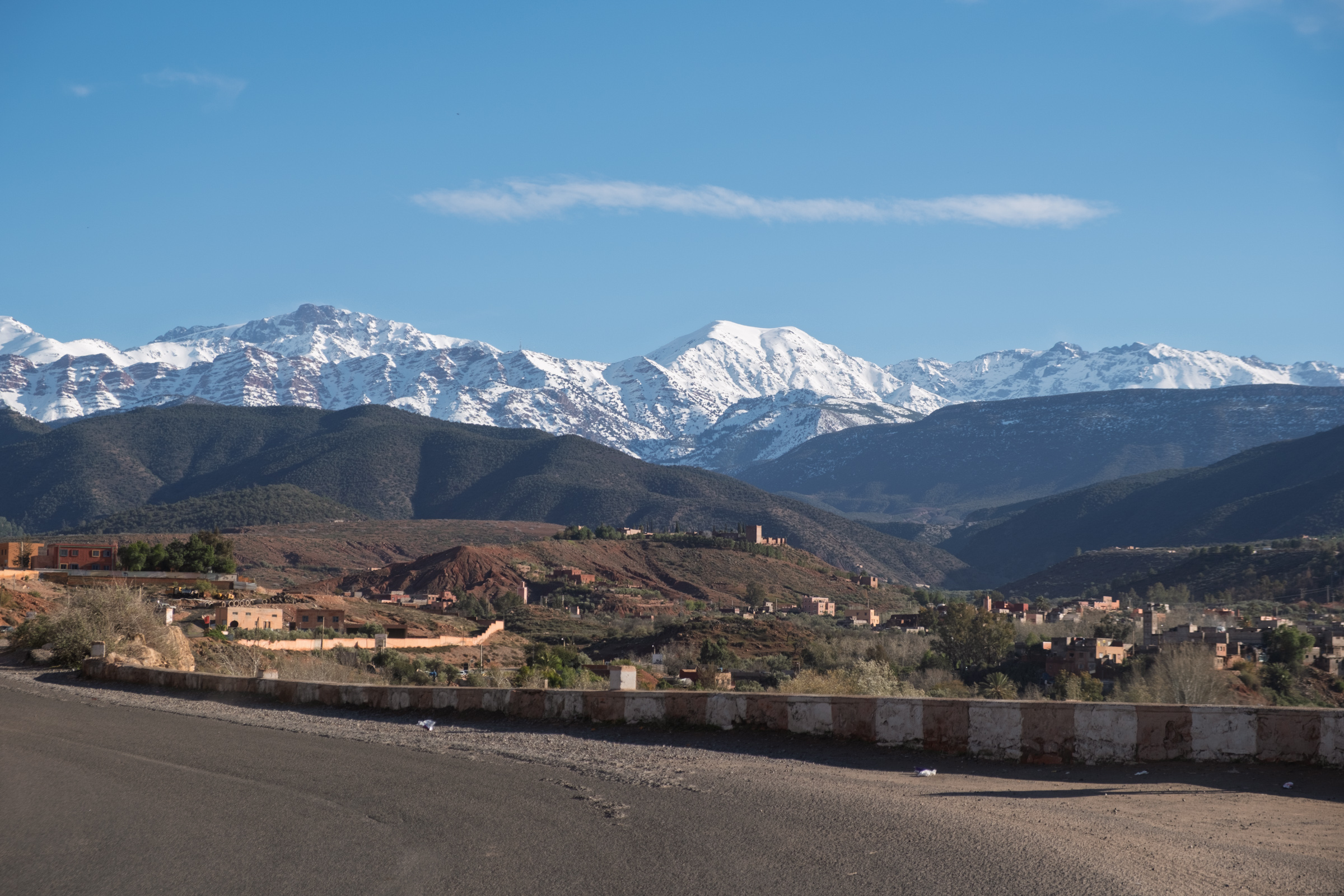 Snow-capped mountains towering over a small town, capturing the scale of the Atlas foothills.
