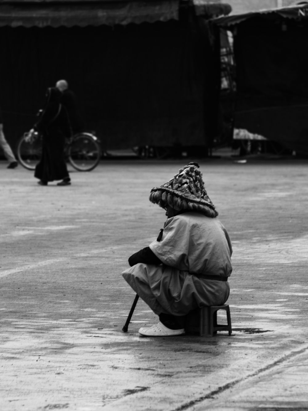 A traditional water seller in full costume sits alone on a low stool in the middle of Djemaa el-Fna, his ornate hat and baggy robes an island of colour in the grey morning. The square has yet to fill.